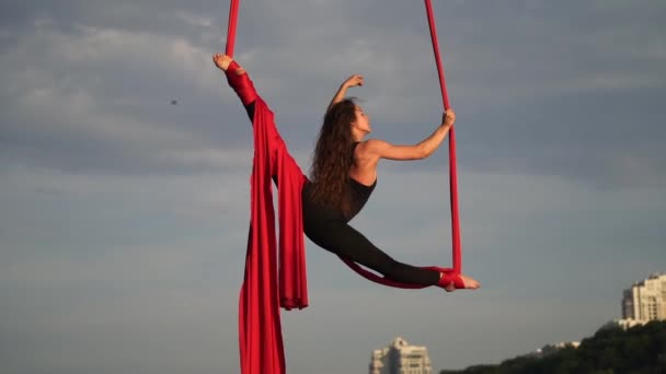Acrobata femminile mostrando la sua flessibilità e si divide con seta aerea rossa sullo sfondo del cielo. Concetto di grazia, movimento e bellezza — Video Stock