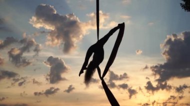 Kadın sirk sanatçısının silueti esnekliğini gösteriyor ve dramatik gökyüzü arka planında kırmızı ipekle ağır çekimde ayrılıyor. Sağlıklı yaşam tarzı kavramı 