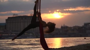 Kadın dansçının silueti esnekliğini gösteriyor ve yavaş çekimde dramatik bir gökyüzü sırasında şehrin arka planında kırmızı havadan ipekle ayrılıyor. Sağlıklı yaşam tarzı kavramı.