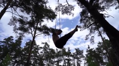 Adam yeşil parkta TRX veya hava kayışlarıyla yavaş çekimde jimnastik yapıyor. Sağlıklı yaşam tarzı ve sağlık