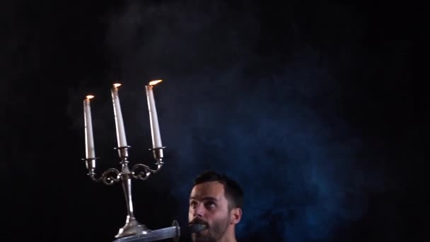 입에 칼을 쥐고 있는 서커스 미술가가 촛대로 풍선을 불어서 균형을 유지하고 있는 모습 — 비디오