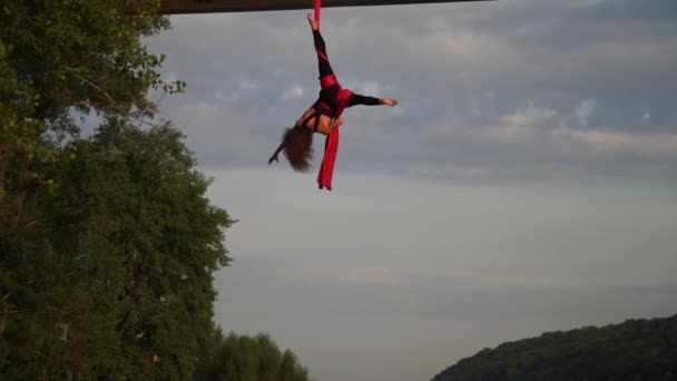 Silhouette einer flexiblen weiblichen Akrobatin, die einen verrückten und gefährlichen Trick auf roter Antennenseide macht. Der Hintergrund des Sonnenuntergangs ist Zeitlupe. Konzept von Gefahr, Risiko — Stockvideo