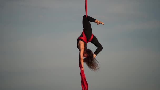 Női akrobata mutatja rugalmasságát, és hasít piros légi selyem az ég hátterében lassított felvétel. A kegyelem, a mozgás és a szépség fogalma — Stock videók