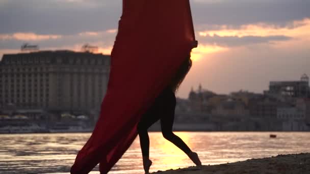 Silhouette de danseuse montrant sa souplesse et se divise avec de la soie aérienne rouge sur le fond du paysage urbain pendant le ciel dramatique au ralenti. Concept de passion, de désir et d'attraction — Video