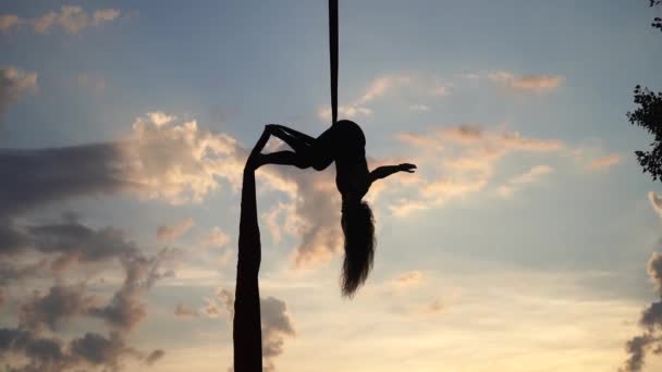 Artista de circo femenino mostrando su flexibilidad y se divide con seda aérea roja en el fondo del cielo. Concepto de estilo de vida saludable — Vídeos de Stock