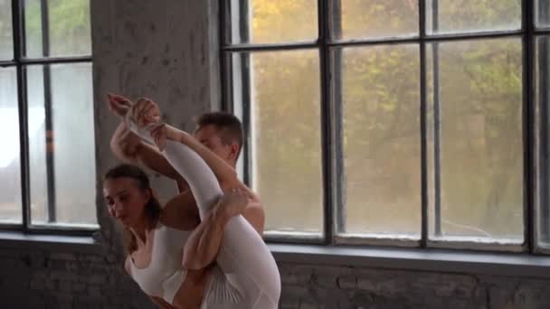 Acrobatic duet robi ładną pozę na tle ogromnych okien z jesiennymi drzewami pomarańczowymi na zewnątrz. Pojęcie relacji, szczęścia i zaufania — Wideo stockowe