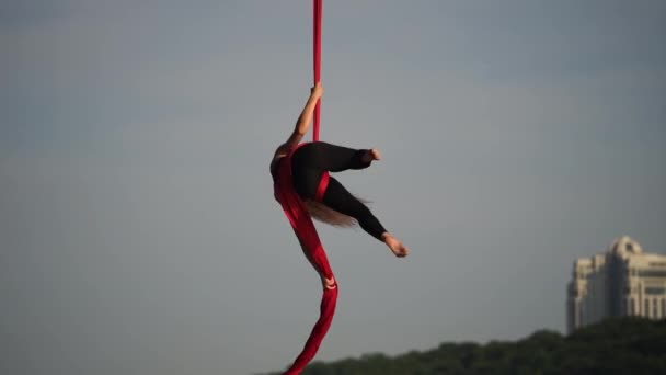 Kvinnlig akrobat visar sin flexibilitet och delar sig med rött antenn silke på himlen bakgrunden är slow motion. Begreppet nåd, rörelse och skönhet — Stockvideo