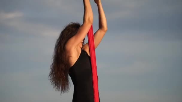 Kvinnlig cirkusartist visar sin flexibilitet och delar sig med rött antenn silke på himlen bakgrund. Begreppet hälsosam livsstil — Stockvideo
