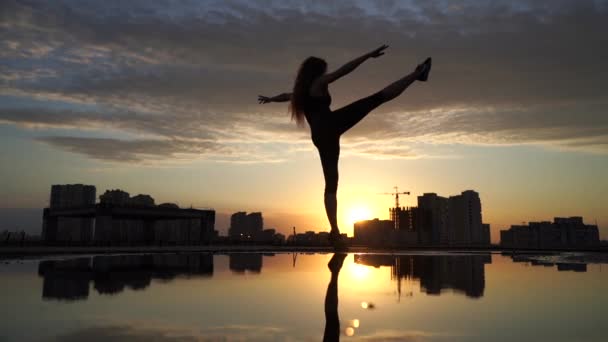 水面に映る街並みを背景に、日没時にゆっくりとした動きで女性の柔軟な踊り。自由と幸福の概念 — ストック動画