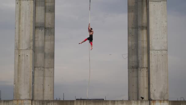 Strong and muscular circus artist performing on the aerial rope outdoor between two concrete columns on the sky background, Concept of courage, control and endurance — Stock Video