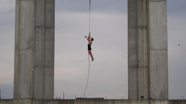 Güçlü ve kaslı sirk sanatçısı gökyüzünde arka planda iki beton sütun arasında hava ipinde gösteri yapıyor güç, risk ve tehlike kavramı. — Stok video