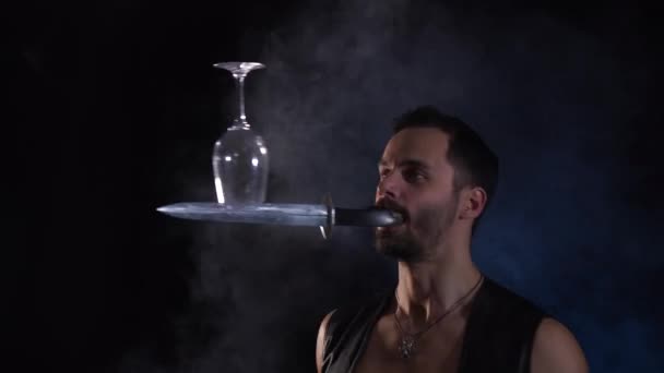 En man håller en kniv i munnen, kastar och håller sitt glas i balans. Unik cirkusfärdighet. — Stockvideo