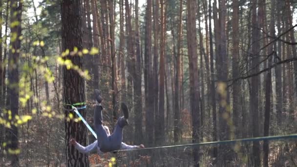 男ジャンプやスローモーションで森の中でスラックライン上でトリックを行う — ストック動画