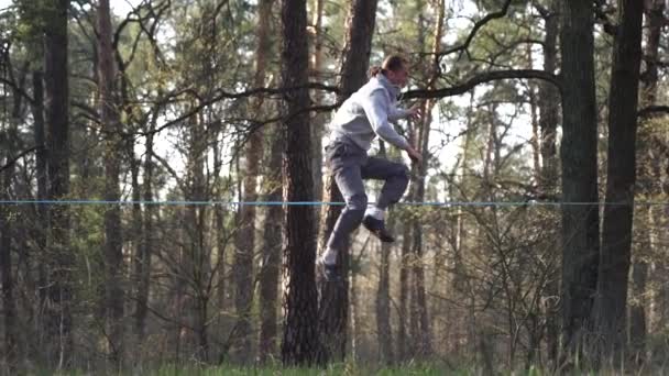 Man springen en doen trucs op slackline in het bos in slow motion — Stockvideo