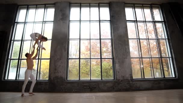 Acrobatic duet co trudne sztuczki na tle ogromnych okien z jesiennych drzew pomarańczowych na zewnątrz. Pojęcie wsparcia i relacji — Wideo stockowe