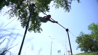 Mavi gökyüzü arka planında yatay çubukta jimnastik numaraları yapan kaslı adamın silueti. Sağlıklı yaşam tarzı, jimnastik ve egzersiz kavramı 