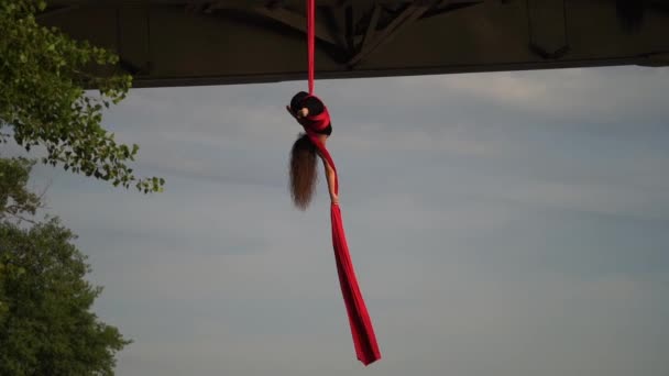 Zirkusartistin, die ihre Flexibilität zeigt und sich mit roter Antennenseide auf dem Himmelshintergrund teilt, ist Zeitlupe. Konzept eines gesunden Lebensstils — Stockvideo