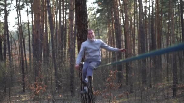 Uomo che salta e fa trucchi su slackline nella foresta al rallentatore — Video Stock