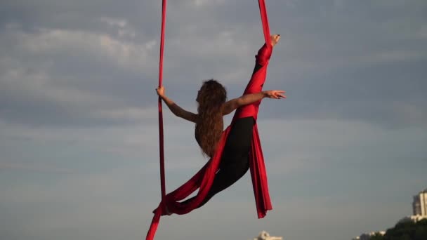 Kobieta akrobatka wykazująca się elastycznością i rozszczepia się czerwonym powietrznym jedwabiem na tle nieba jest w zwolnionym tempie. Pojęcie łaski, ruchu i piękna — Wideo stockowe