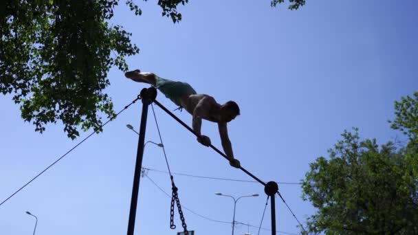 Sylwetka muskularnego mężczyzny wykonującego gimnastyczne sztuczki na poziomym drążku w zwolnionym tempie na tle niebieskiego nieba. Koncepcja kontroli, ruchu i koncentracji — Wideo stockowe