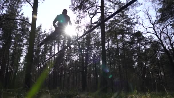 男ジャンプやスローモーションで森の中でスラックライン上でトリックを行う — ストック動画
