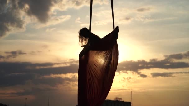 Silhouette of Female Circus Artist viser sin fleksibilitet og deler seg med rød antenne silke på den dramatiske himmelbakgrunnen i sakte film. Bevegelsesbegrep og bevegelse – stockvideo