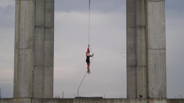 Sterke en gespierde circusartiest die optreedt op het touw buiten tussen twee betonnen zuilen op de achtergrond van de lucht, concept van moed, controle en uithoudingsvermogen — Stockvideo