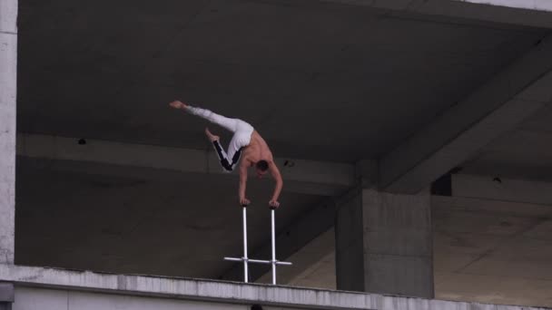 De man houdt de balans aan de ene kant op de circusstokken in het oude verlaten gebouw. Concept van handstand, uitvoering en kunst — Stockvideo