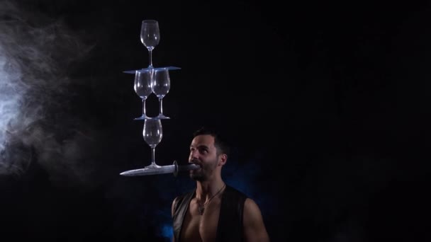 Man hold knife in the mouth and keep in balance wineglasses on it. concentration — Stock Video