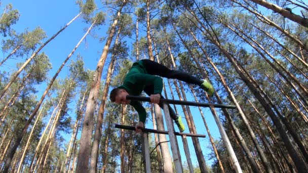Мужчина занимается гимнастикой на параллельных брусьях в лесу. Здоровый образ жизни — стоковое видео