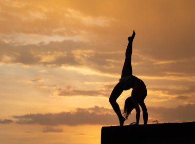 Dramatik günbatımında gökyüzü arka planı üzerinde egzersiz yapan esnek bir kız.