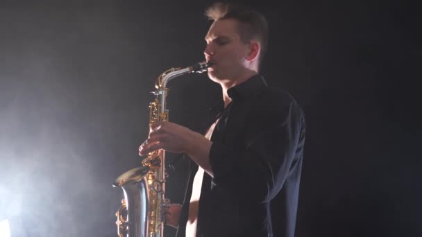 Man wearing black shirt playing on saxophone isolated on smoked background — Stock Video