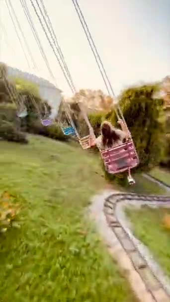 Счастливая девушка-подросток катается на карусели в парке аттракционов сзади. Понятие счастья и радости — стоковое видео