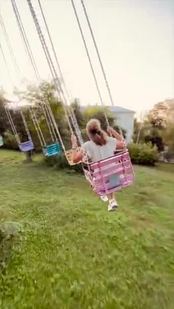 Happy woman teenage girl riding chain carousel swing at amusement park from behind. Concept of happiness and joy — Stock Video