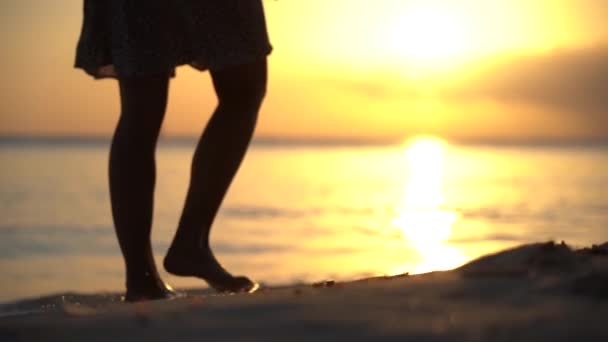 Close-up de mulheres pés em vestido andando sozinho na praia durante o pôr do sol em câmera lenta. Conceito estilo de vida saudável e prazer o momento — Vídeo de Stock