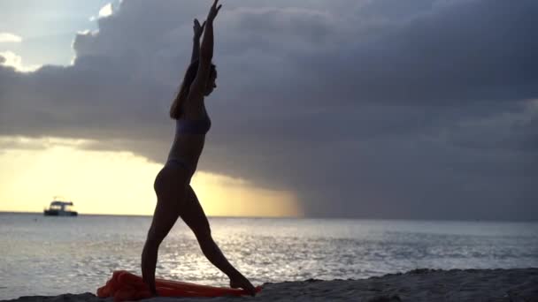 Silhouette de femme à la coupe souple qui se tient debout avec de la soie lors d'un coucher de soleil spectaculaire avec des nuages orageux sur le fond du paysage marin. Concept de bonheur, de liberté et d'insouciance. — Video