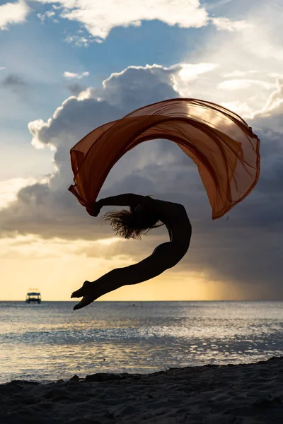 Mujer flexible en forma saltando con seda durante el dramático atardecer con nubes tormentosas. Concepto de individualidad, creatividad y confianza en sí mismo — Foto de Stock