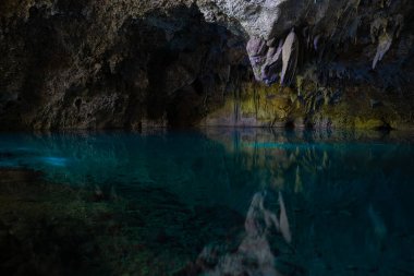 Light descends into the darkness of a submerged cavern with blue lake. Concept of travel and adventure. clipart