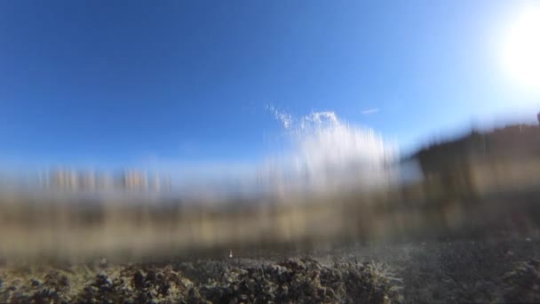 Cresta de una ola de rompientes de mar con salpicaduras en un acantilado de rocas volcánicas hace que la calma, el agua cristalina en la piscina natural áspera y burbujas en cámara lenta con el cielo azul en el fondo — Vídeo de stock