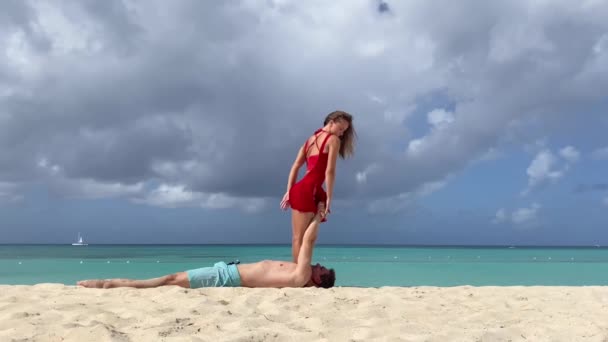 Un tipo con una chica hace trucos acrobáticos en la playa. concepto de relación y unidad — Vídeo de stock