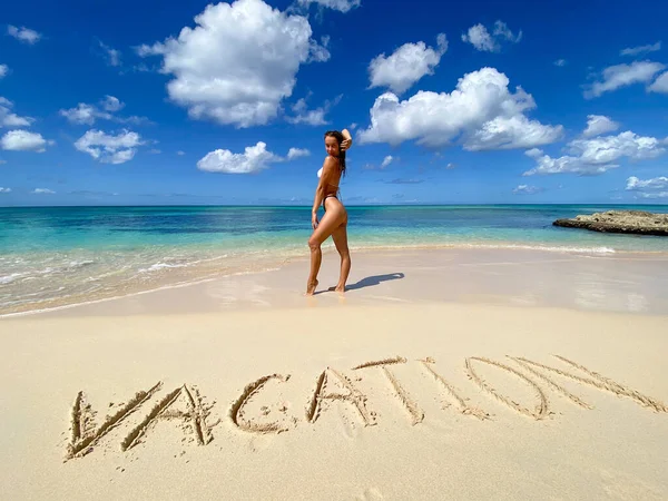 Сексуальна бікіні жінка грає на райському тропічному пляжі з написом на піску. Концепція подорожей та відпусток — стокове фото