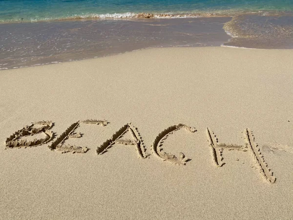 BEACH inskription på sanden med havsvågor och himmel. Begreppet semester och semester — Stockfoto