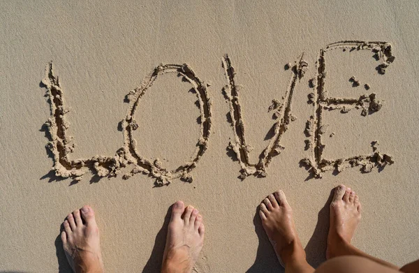 LOVE inscription on summer sandy beach with couples foots near. Relation ship and togetherness concept Stock Photo