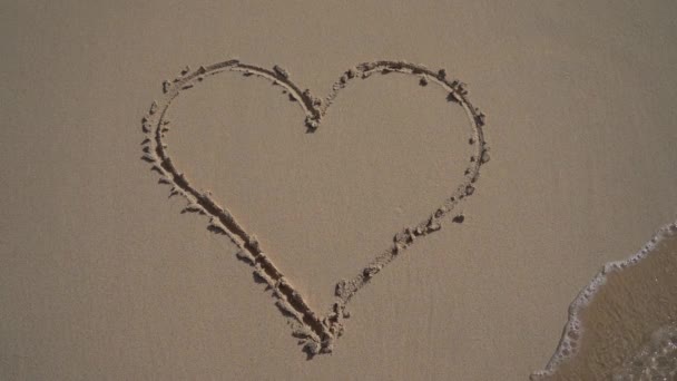 파도가 와서 모래에 있는 하트의 그림을 지우고 있습니다. 이혼 과 결별 개념 — 비디오