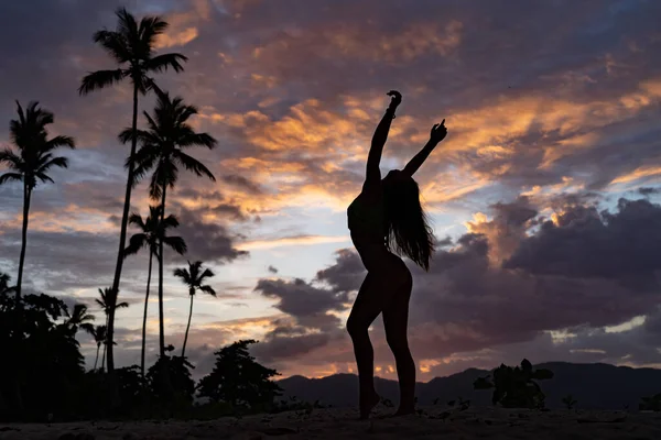 Silueta de mujer durante el atardecer tropical con palmera y nubes dramáticas. Concepto de vacaciones y viajes. — Foto de Stock