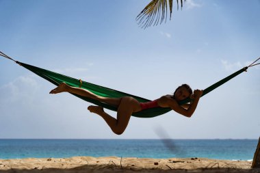 Hamaktaki genç kadın tropik plaja bakıyor. Tatil ve seyahat kavramı 