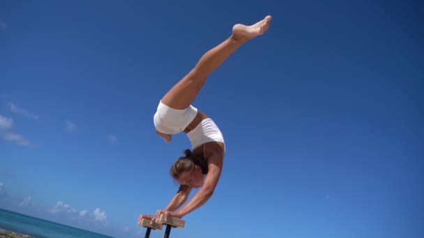 Γυναίκα φορώντας λευκά κάνει handstand στην παραλία με τη θάλασσα. Ατομικότητα, εξαιρετική και πρωτοτυπία. — Αρχείο Βίντεο