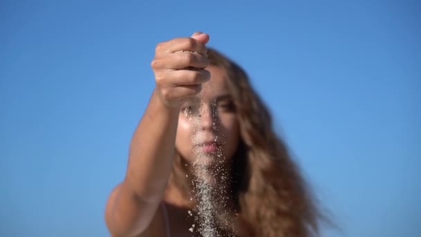 Sand faller gjennom kvinnens fingre med himmelbakgrunn i sakte film. Ferie- og reisebegrep – stockvideo