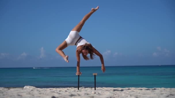 Femme vêtue de blanc faisant handstand sur la plage avec la mer. Mode de vie sain et concept de soins du corps. — Video