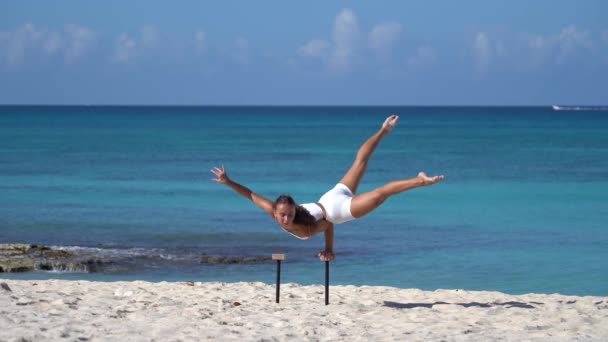 Γυναίκα φορώντας λευκά κάνει handstand στην παραλία με τη θάλασσα. Υγιεινός τρόπος ζωής και φροντίδα του σώματος. — Αρχείο Βίντεο